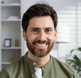 Smiling man in dental office setting wearing olive green shirt.