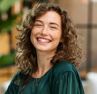 Smiling woman with curly brown hair wearing a teal top in a dental office setting.